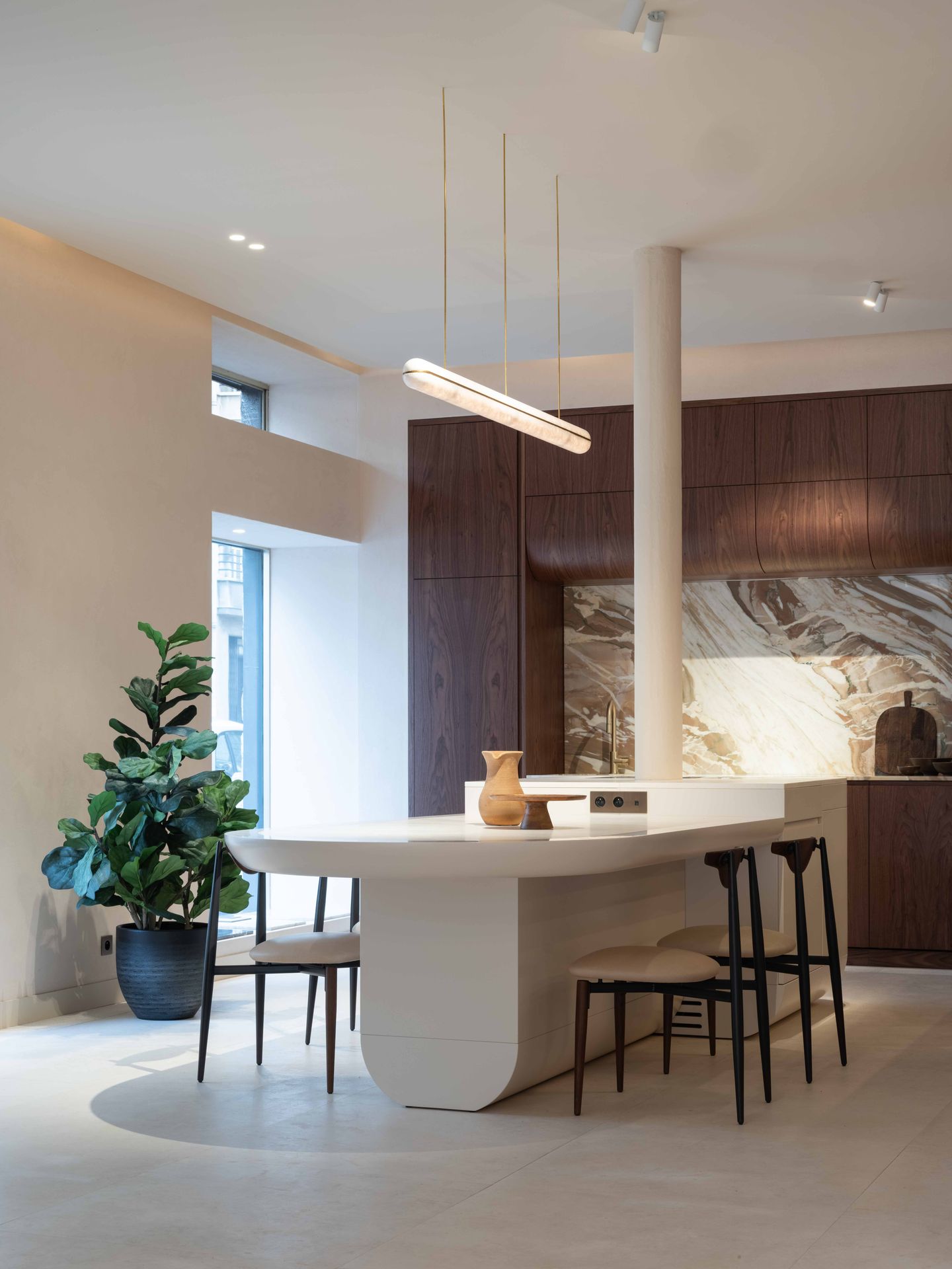 Îlot central aux angles arrondis prolongé en table, cuisine à façades bois foncé et crédence en marbre Calacatta Vagli Rosato
