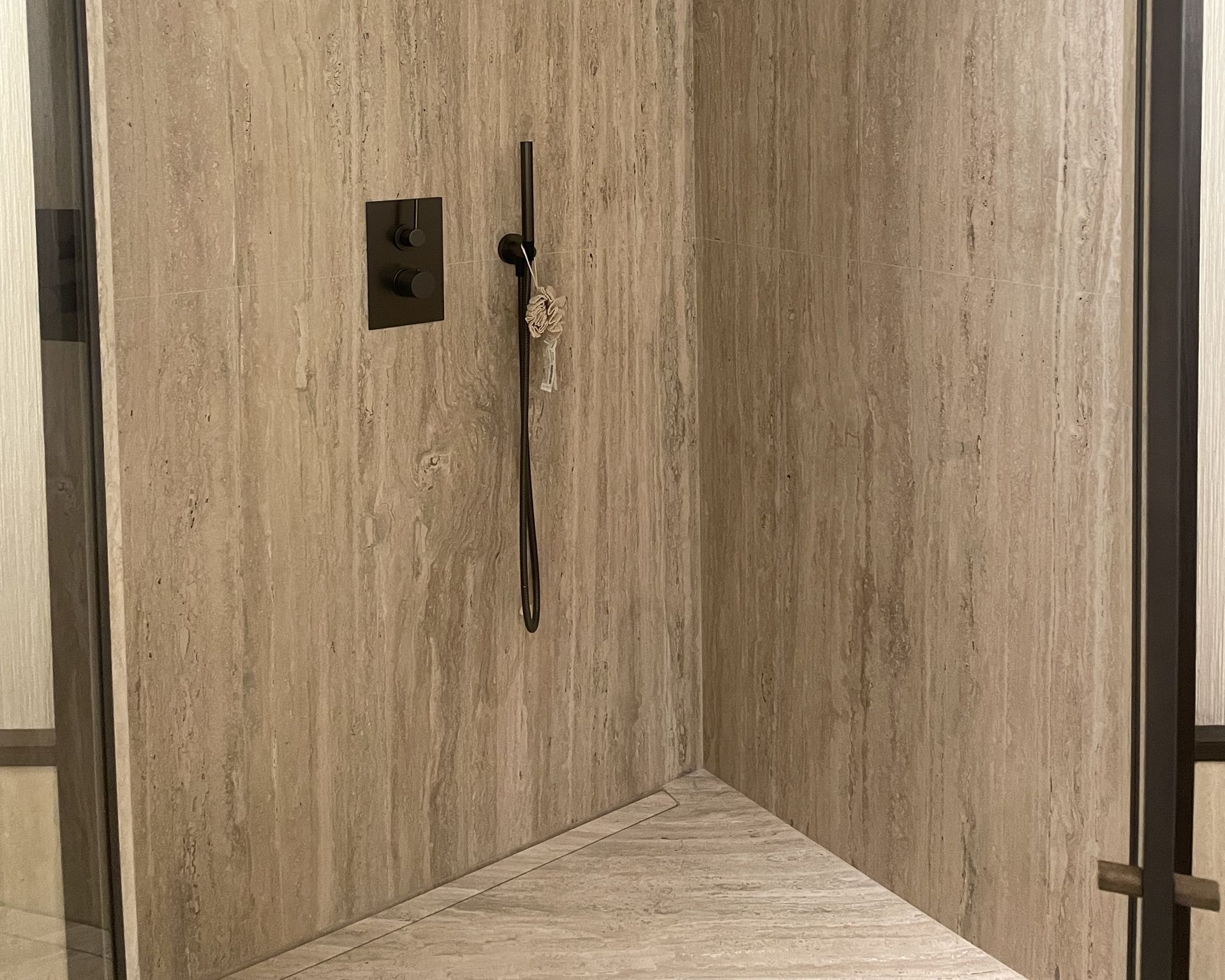 Douche habillée de travertin beige dans une salle de bains à meuble brun foncé