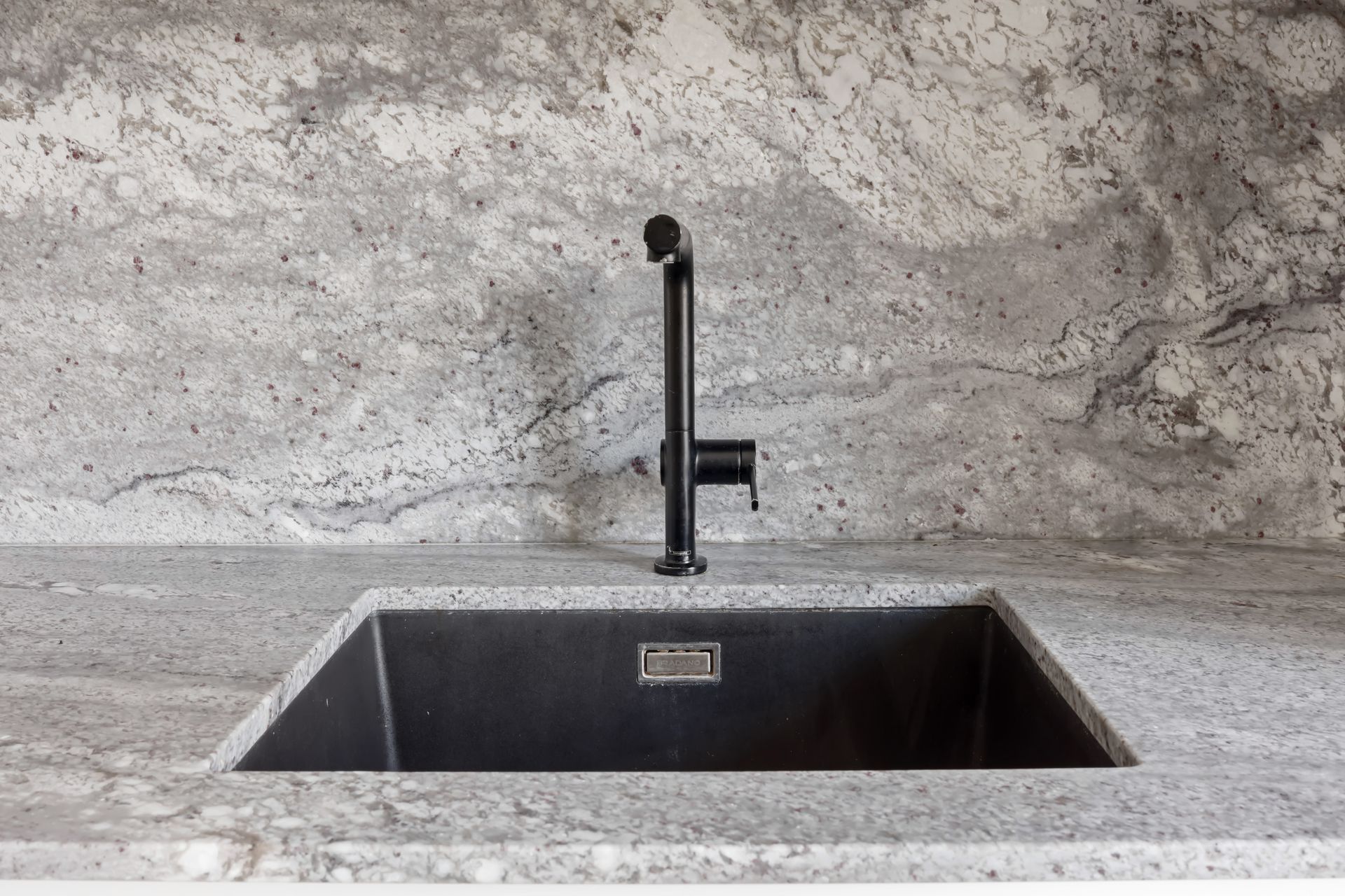 Évier taillé dans un plan de travail gris en granit Sensa Sant Angelo, cuisine à façades blanches et bois clair